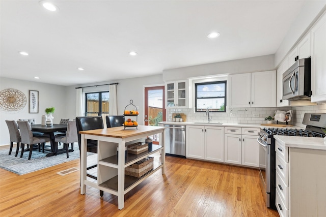 kitchen with a sink, stainless steel appliances, light countertops, light wood-type flooring, and backsplash