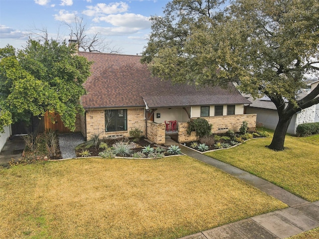 view of front facade featuring a front lawn, a chimney, a shingled roof, and brick siding