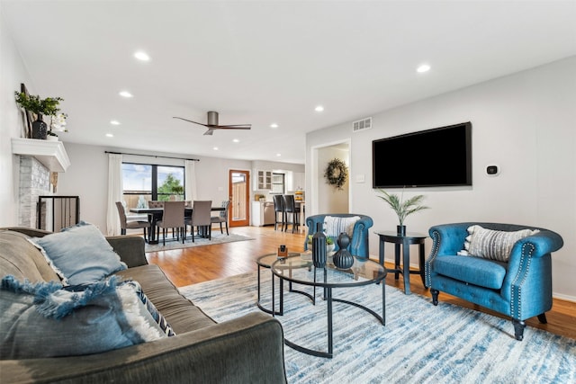 living room featuring baseboards, visible vents, light wood-style floors, a fireplace, and recessed lighting