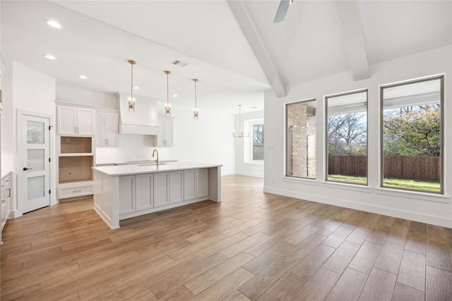 kitchen featuring white cabinetry, ceiling fan, hanging light fixtures, backsplash, and an island with sink