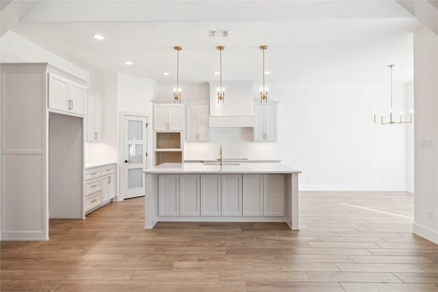 kitchen featuring sink, white cabinetry, hanging light fixtures, and a kitchen island with sink