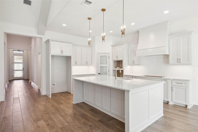 kitchen featuring white cabinets, custom range hood, sink, and an island with sink