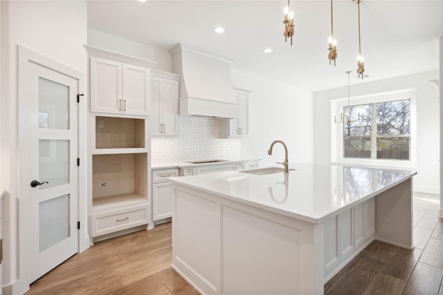 kitchen with custom range hood, white cabinetry, sink, and decorative light fixtures