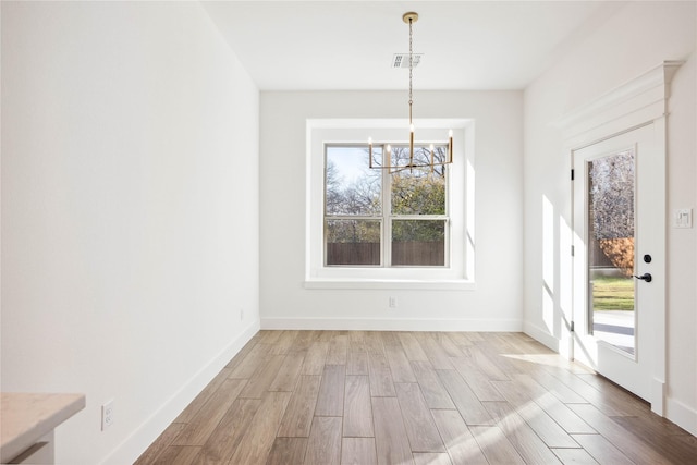 unfurnished dining area featuring light wood-type flooring and a notable chandelier