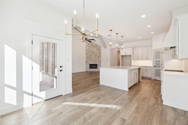 kitchen with pendant lighting, a kitchen island with sink, vaulted ceiling, tasteful backsplash, and white cabinetry