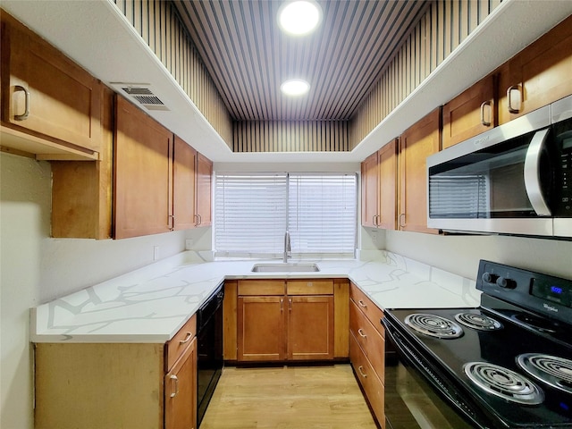 kitchen with black appliances, light hardwood / wood-style floors, light stone counters, and sink