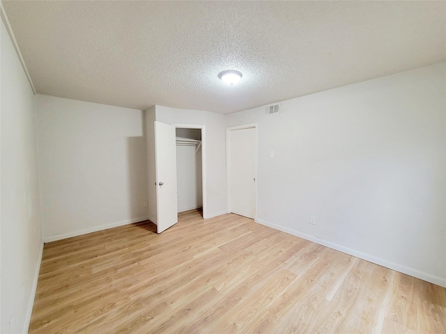 unfurnished bedroom featuring a textured ceiling, light hardwood / wood-style floors, and a closet