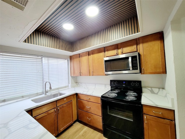 kitchen with stainless steel microwave, visible vents, brown cabinetry, a sink, and black range with electric cooktop