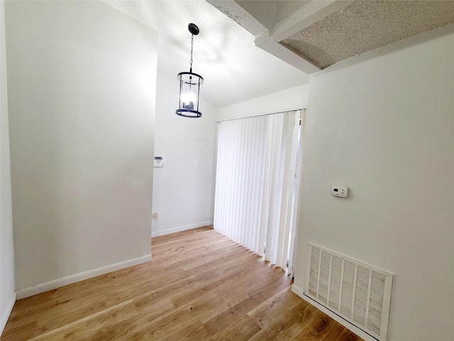 interior space featuring light wood finished floors, baseboards, visible vents, vaulted ceiling, and a textured ceiling