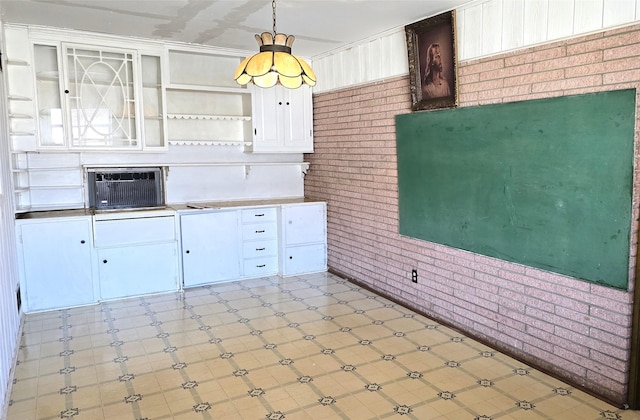 kitchen featuring white cabinets, hanging light fixtures, and brick wall