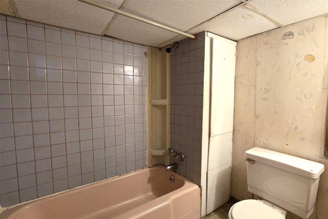 bathroom featuring a drop ceiling, toilet, and tiled shower / bath