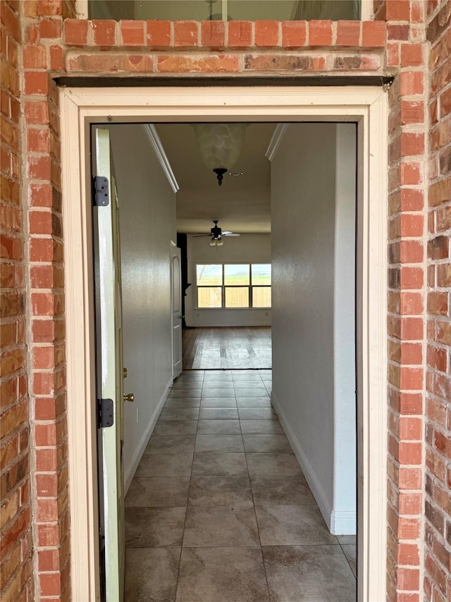 hallway with brick wall, tile patterned flooring, and baseboards