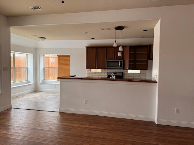 kitchen with kitchen peninsula, stove, tasteful backsplash, pendant lighting, and hardwood / wood-style flooring