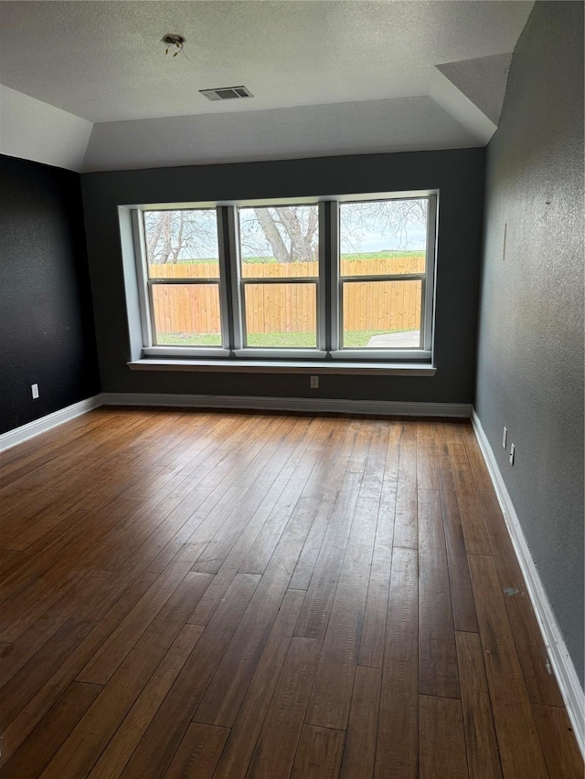 spare room featuring hardwood / wood-style flooring, lofted ceiling, and a textured ceiling