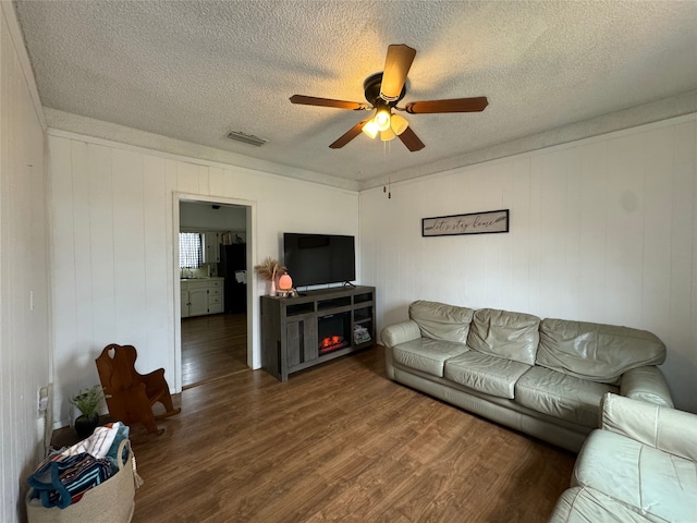 living room with dark hardwood / wood-style floors, a textured ceiling, ceiling fan, and wood walls