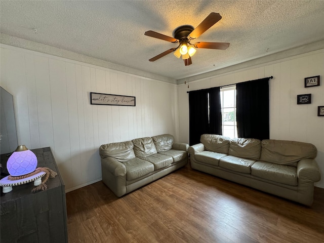 living room featuring ceiling fan, dark wood-type flooring, a textured ceiling, and wooden walls