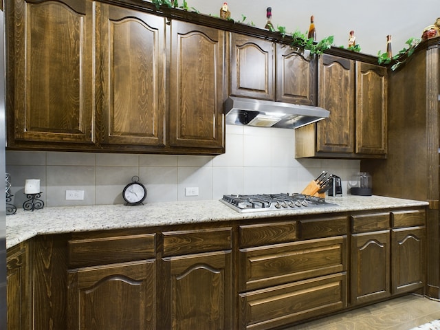 kitchen featuring dark brown cabinetry, light stone counters, decorative backsplash, and stainless steel gas cooktop