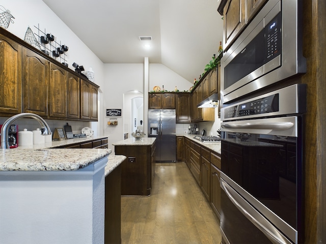 kitchen with hardwood / wood-style floors, dark brown cabinetry, appliances with stainless steel finishes, a center island, and vaulted ceiling