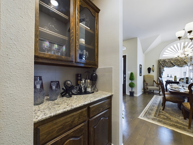 bar with a notable chandelier, dark brown cabinetry, light stone counters, and dark hardwood / wood-style floors