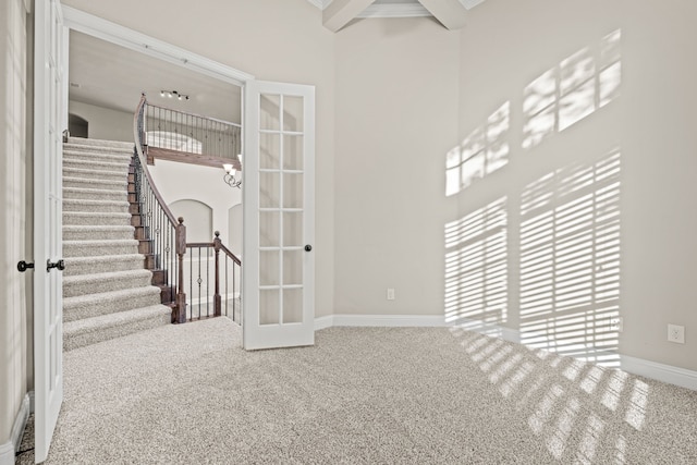 carpeted spare room featuring beamed ceiling and french doors