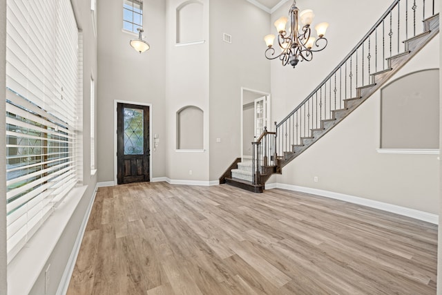 foyer entrance featuring a towering ceiling, light hardwood / wood-style floors, and a notable chandelier