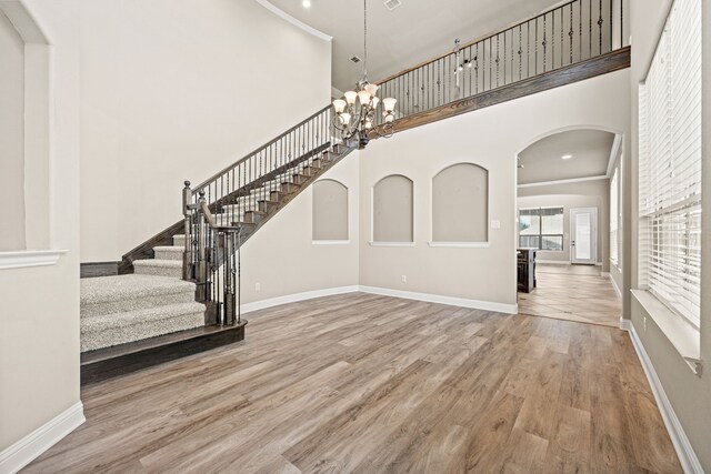 foyer entrance featuring crown molding, a high ceiling, a notable chandelier, and light wood-type flooring