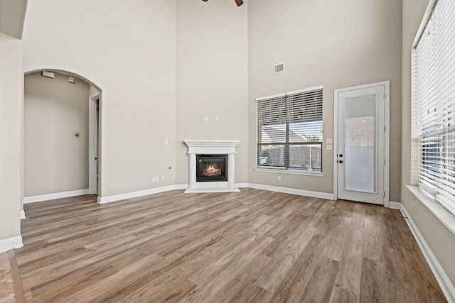 unfurnished living room featuring ceiling fan, a towering ceiling, and light hardwood / wood-style floors