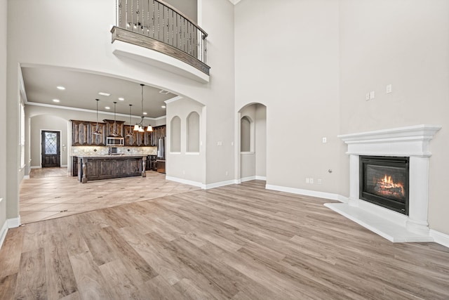 unfurnished living room featuring ornamental molding, a towering ceiling, and light hardwood / wood-style flooring