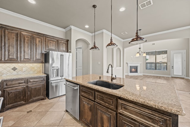 kitchen with dark brown cabinetry, sink, light stone counters, a kitchen island with sink, and appliances with stainless steel finishes