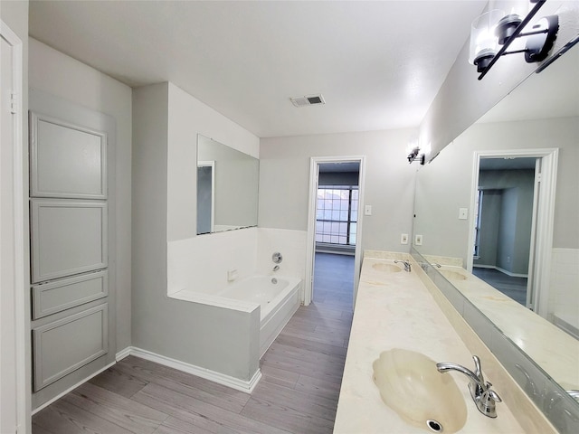 bathroom featuring tiled tub, vanity, and wood-type flooring