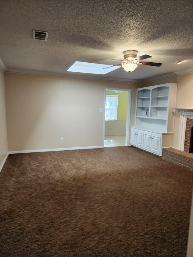 unfurnished living room featuring a skylight, a brick fireplace, a textured ceiling, carpet flooring, and ceiling fan