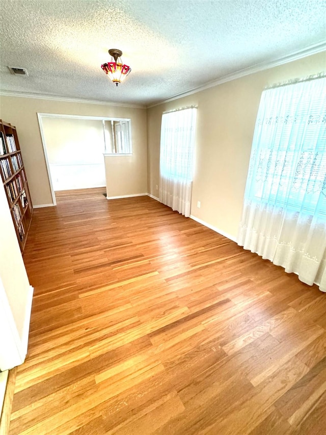 spare room with ornamental molding, a textured ceiling, and light wood-type flooring