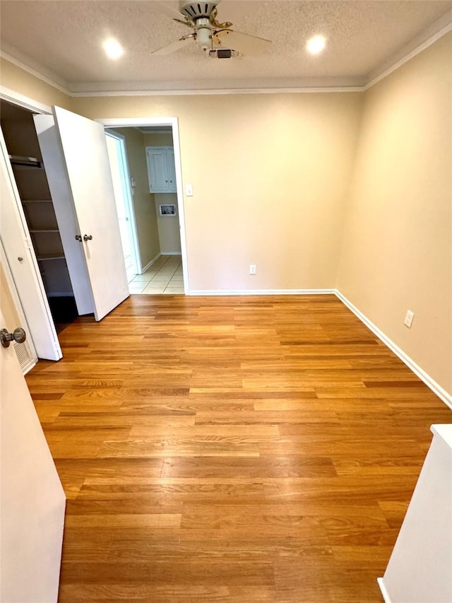 empty room with ornamental molding, ceiling fan, a textured ceiling, and light wood-type flooring