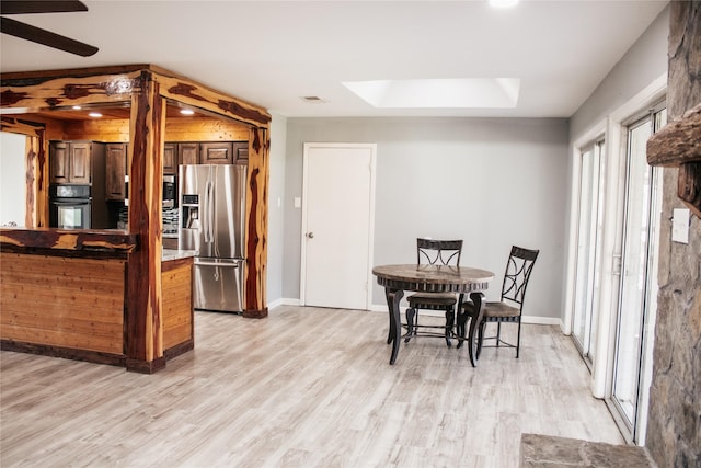 kitchen featuring a skylight, a raised ceiling, ceiling fan, stainless steel appliances, and light wood-type flooring