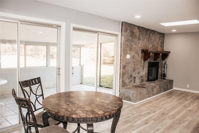 dining area with a stone fireplace, a skylight, and light hardwood / wood-style floors