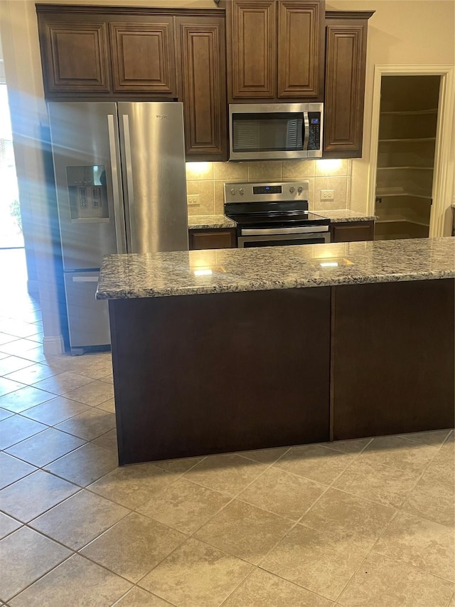 kitchen with backsplash, dark brown cabinetry, light stone countertops, and stainless steel appliances