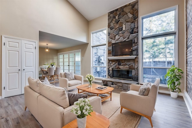 living room with high vaulted ceiling, a stone fireplace, and wood finished floors