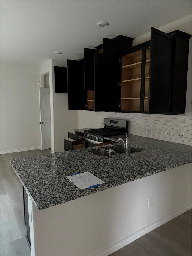 kitchen with kitchen peninsula, stainless steel gas range oven, sink, and stone countertops