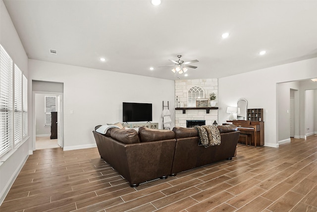 living room featuring a stone fireplace, dark wood-type flooring, and ceiling fan