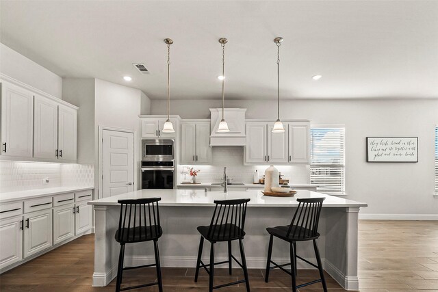 kitchen featuring appliances with stainless steel finishes, a center island with sink, and decorative light fixtures