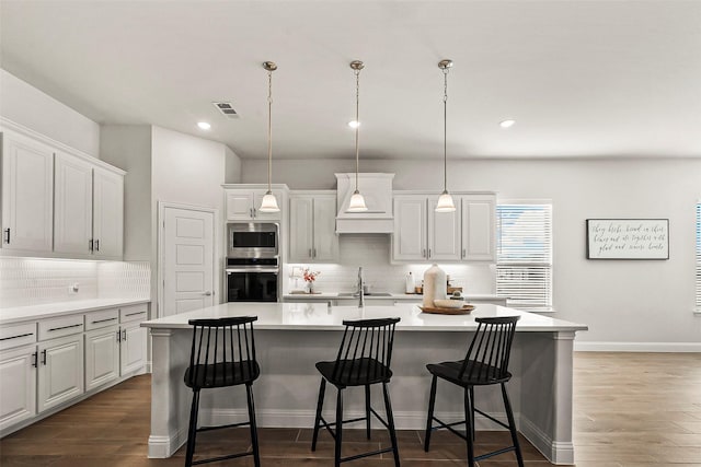 kitchen with stainless steel appliances, decorative light fixtures, and a center island with sink