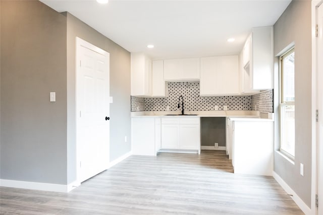 kitchen featuring sink, backsplash, white cabinets, and light wood-type flooring