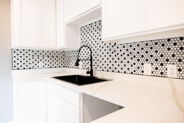 kitchen featuring white cabinetry, sink, light stone counters, and decorative backsplash