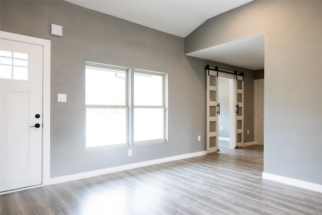 entryway featuring vaulted ceiling, a barn door, plenty of natural light, and light hardwood / wood-style floors