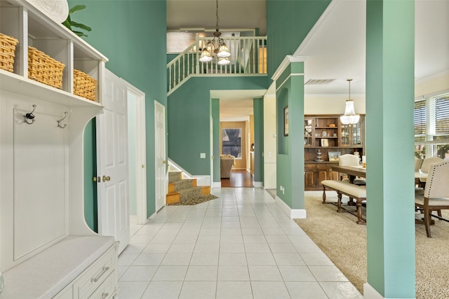 mudroom featuring a chandelier, light colored carpet, a high ceiling, and ornamental molding