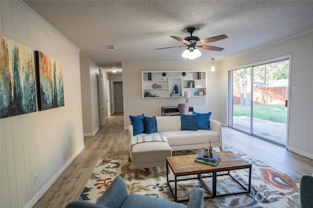 living room featuring ceiling fan, wood walls, light wood-type flooring, and crown molding