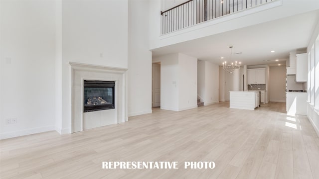 unfurnished living room featuring a chandelier, a high ceiling, light hardwood / wood-style floors, and a tiled fireplace