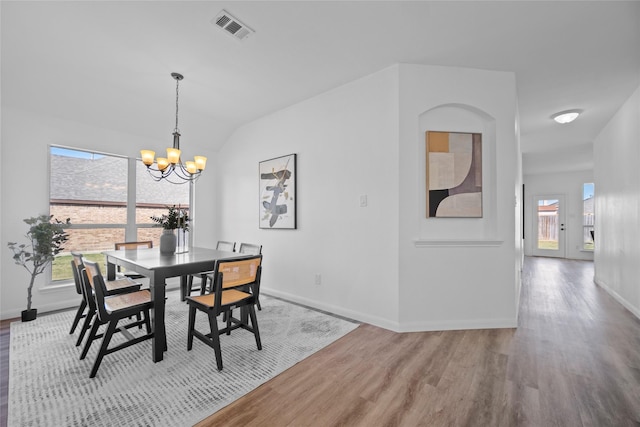 dining space with light hardwood / wood-style floors, vaulted ceiling, and a notable chandelier