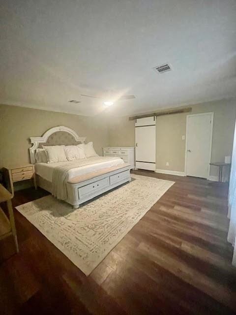 bedroom with a barn door and dark hardwood / wood-style floors