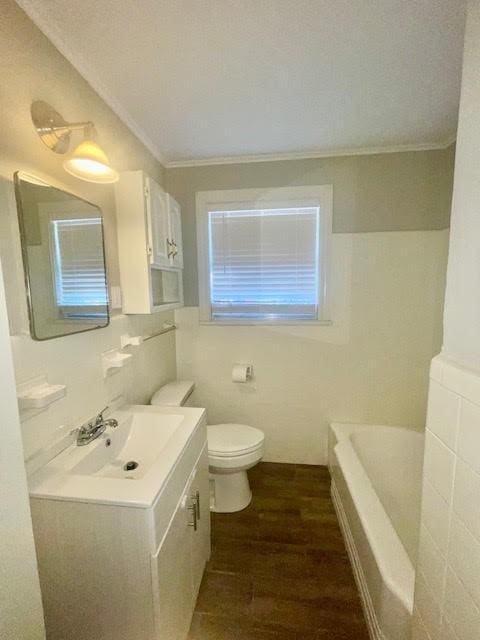 bathroom with ornamental molding, vanity, a bath, wood-type flooring, and toilet